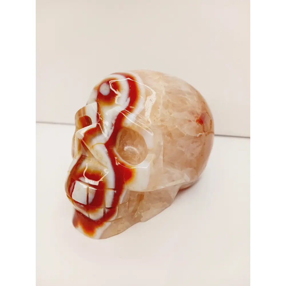Carnelian skull with vibrant orange-red hues and natural banding, carved and displayed on a white background.