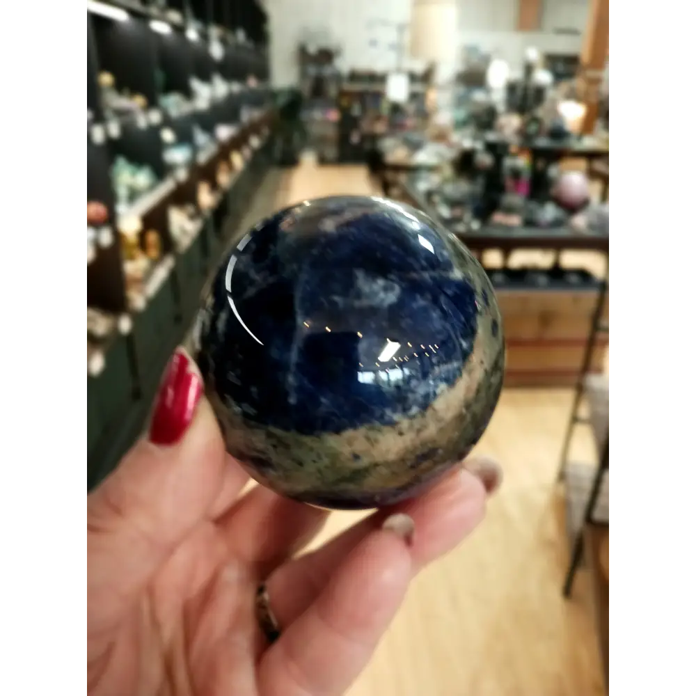 Hand-polished Sodalite sphere featuring deep blue hues with natural white marbling, displayed on a white background.