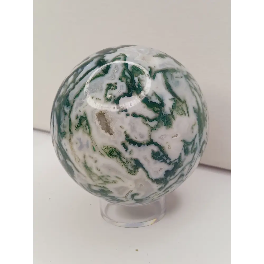 Moss Agate sphere with deep green swirls and sparkling druzy pocket, displayed on a white background.