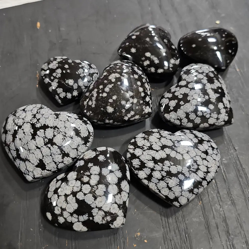Hand-polished snowflake obsidian hearts and palmstones, featuring black stone with white snowflake patterns, displayed on a white background. Perfect for grounding, protection, and gentle transformation.