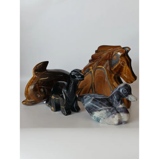 Assorted hand-carved animal figurines made from Blue Tiger’s Eye, Fluorite, and Tiger’s Eye crystals, each featuring unique colors and patterns, displayed on a white background.