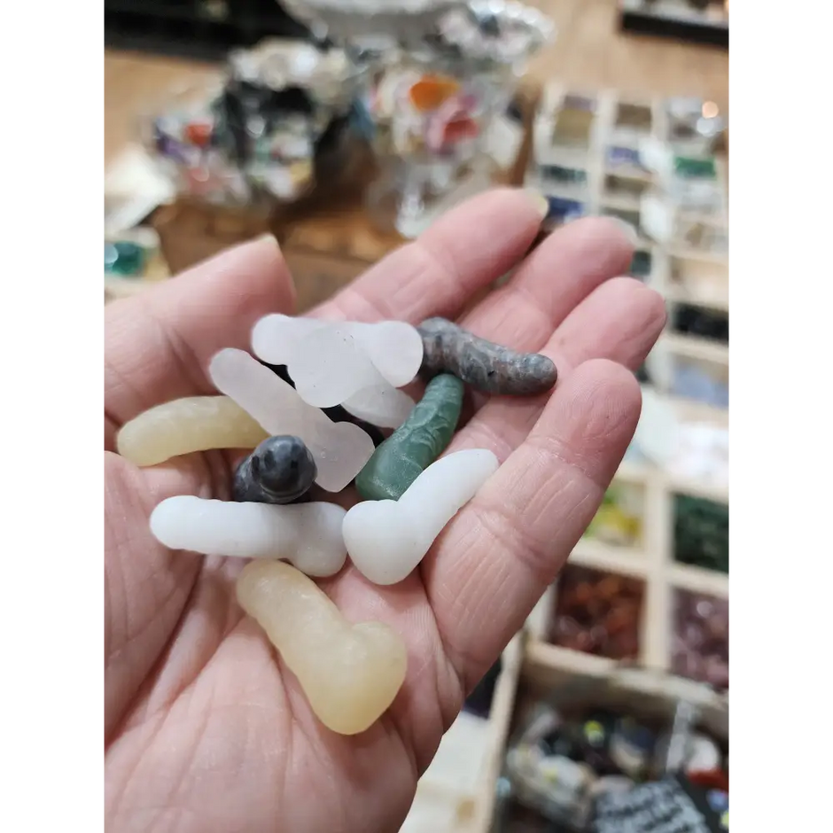 Assorted 1 inch penis-shaped crystal carvings in various colors and stones, hand-carved and displayed on a white background. Perfect for playful energy, empowerment, and root chakra healing.