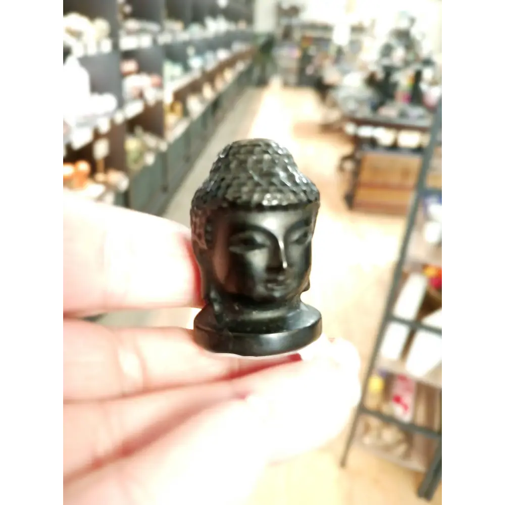 Hand-carved 1 1/2 inch tall Buddha head figurines in assorted crystal materials such as amethyst, rose quartz, clear quartz, and jade, displayed on a white background.