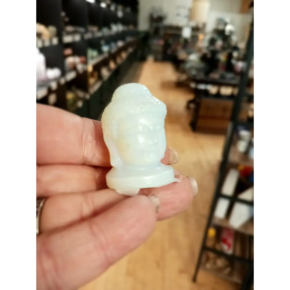 Hand-carved 1 1/2 inch tall Buddha head figurines in assorted crystal materials such as amethyst, rose quartz, clear quartz, and jade, displayed on a white background.