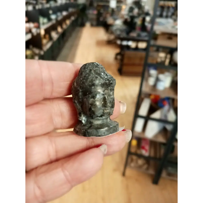 Hand-carved 1 1/2 inch tall Buddha head figurines in assorted crystal materials such as amethyst, rose quartz, clear quartz, and jade, displayed on a white background.
