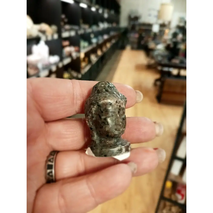 Hand-carved 1 1/2 inch tall Buddha head figurines in assorted crystal materials such as amethyst, rose quartz, clear quartz, and jade, displayed on a white background.