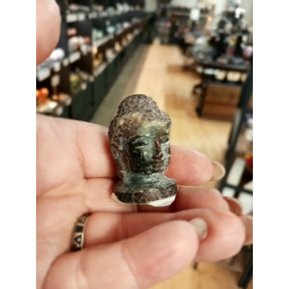 Hand-carved 1 1/2 inch tall Buddha head figurines in assorted crystal materials such as amethyst, rose quartz, clear quartz, and jade, displayed on a white background.