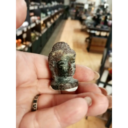 Hand-carved 1 1/2 inch tall Buddha head figurines in assorted crystal materials such as amethyst, rose quartz, clear quartz, and jade, displayed on a white background.