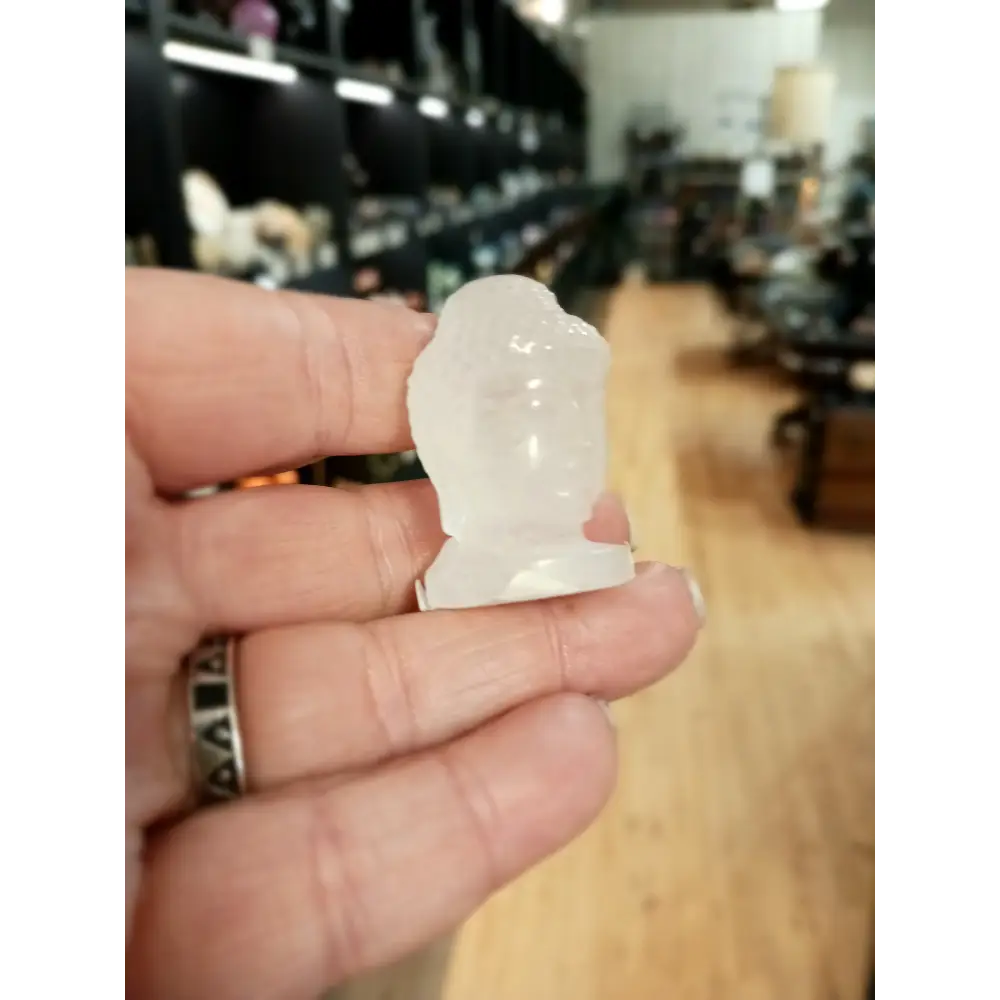 Hand-carved 1 1/2 inch tall Buddha head figurines in assorted crystal materials such as amethyst, rose quartz, clear quartz, and jade, displayed on a white background.