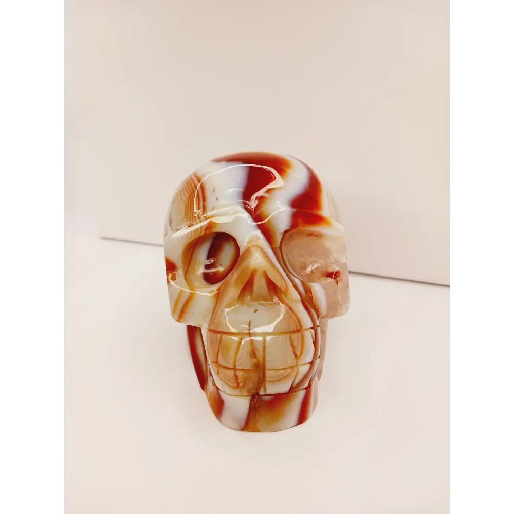 Carnelian skull with vibrant orange-red hues and natural banding, carved and displayed on a white background.