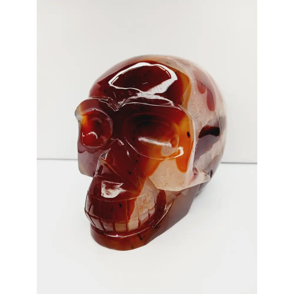 Carnelian skull with vibrant orange-red hues and natural banding, carved and displayed on a white background.