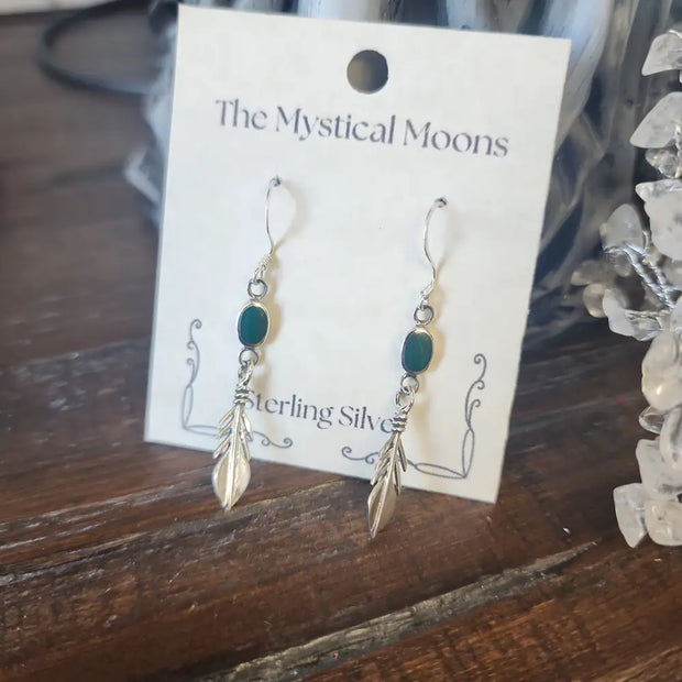 Sterling silver feather earrings featuring vibrant malachite stones, displayed on a white background. Perfect for transformation, protection, and spiritual freedom.
