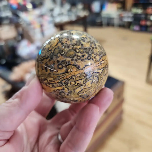 Hand-polished Leopard Skin Jasper sphere featuring bold, spotted patterns in earthy tones, displayed on a white background.