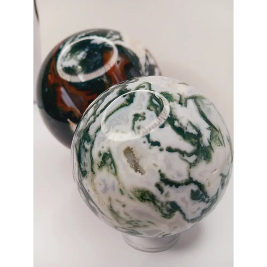 Moss Agate sphere with deep green swirls and sparkling druzy pocket, displayed on a white background.
