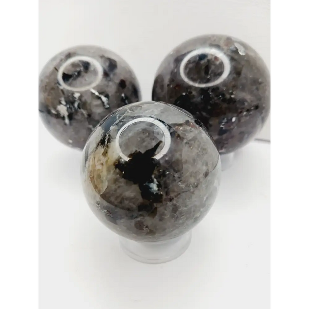 Quartz, garnet, tourmaline, and mica sphere, polished with clear, red, black, and shimmering inclusions, displayed on a white background.