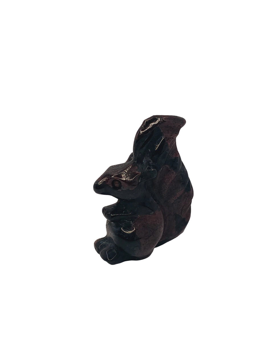 A small dark brown frog figurine with metallic silver accents on its eyes and back, resting on a plain white surface.