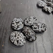 Hand-polished snowflake obsidian hearts and palmstones, featuring black stone with white snowflake patterns, displayed on a white background. Perfect for grounding, protection, and gentle transformation.