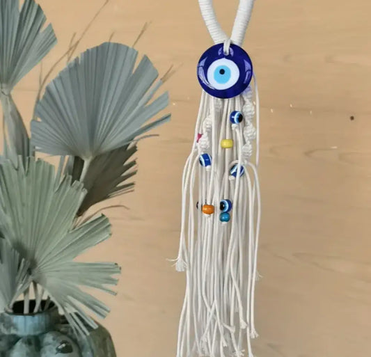 Decorative hanging with tassels and an eye-shaped charm next to a plant on a wooden surface