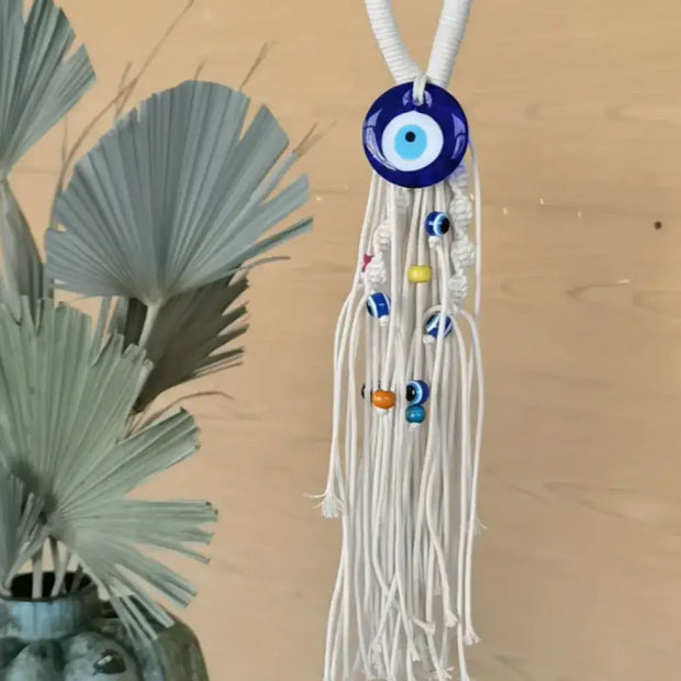 Decorative hanging with tassels and an eye-shaped charm next to a plant on a wooden surface