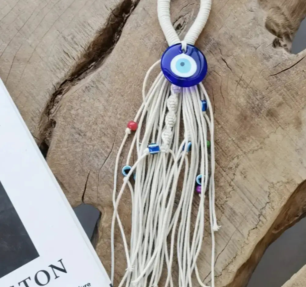 Decorative hanging with white strings and blue circular beads on a wooden surface