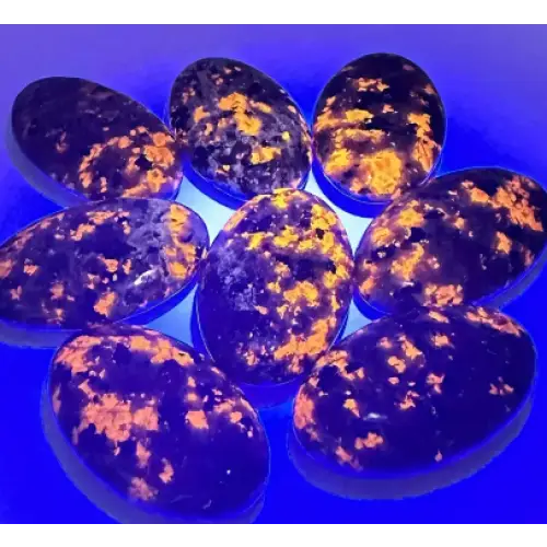 Hand-polished Yooperlite palmstone, glowing with vibrant orange and yellow patterns under UV light, displayed on a white background. Perfect for creativity, transformation, and mystical energy.